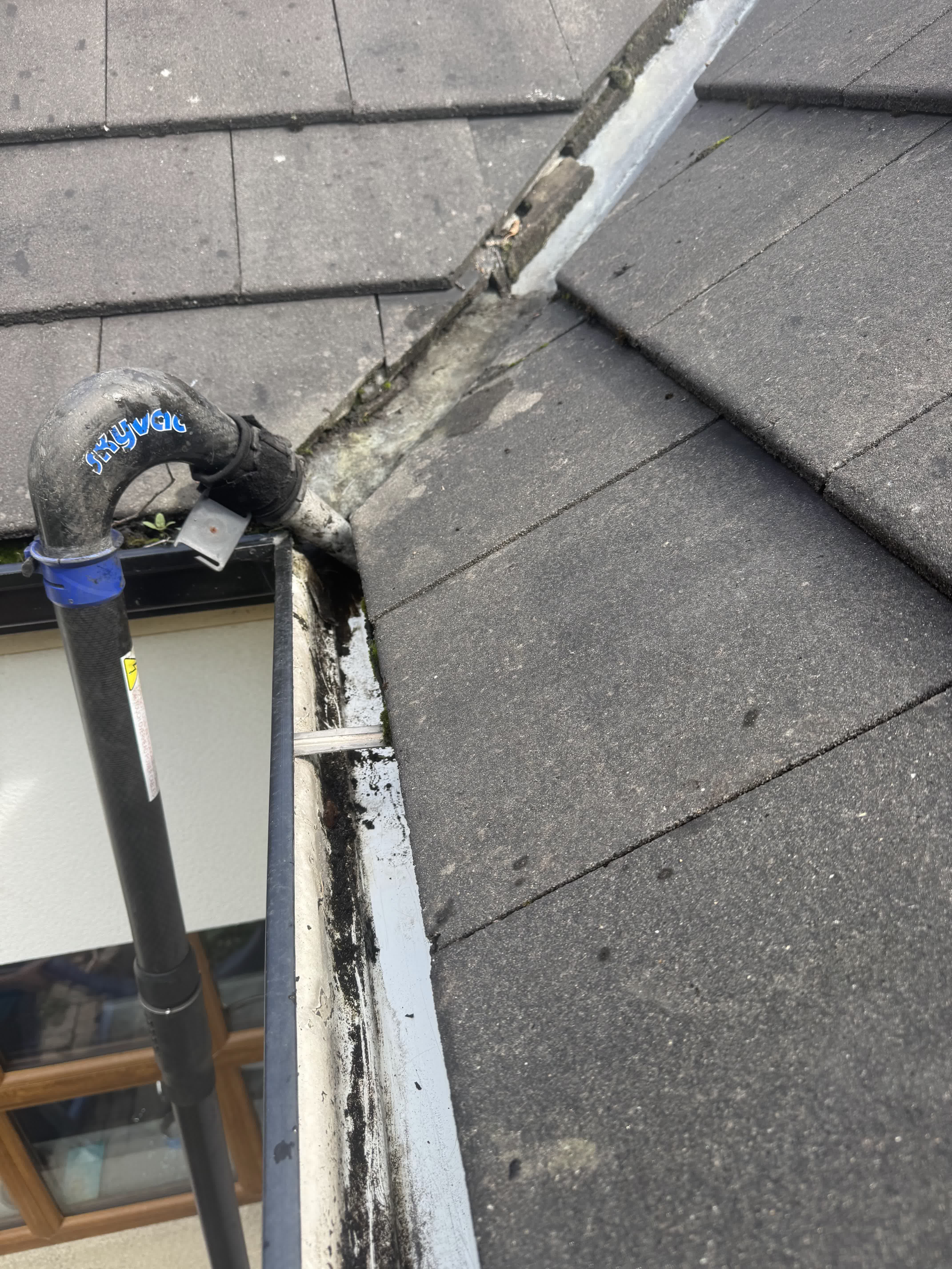 The same gutter after clearing, with the vacuum nozzle still in the gutter